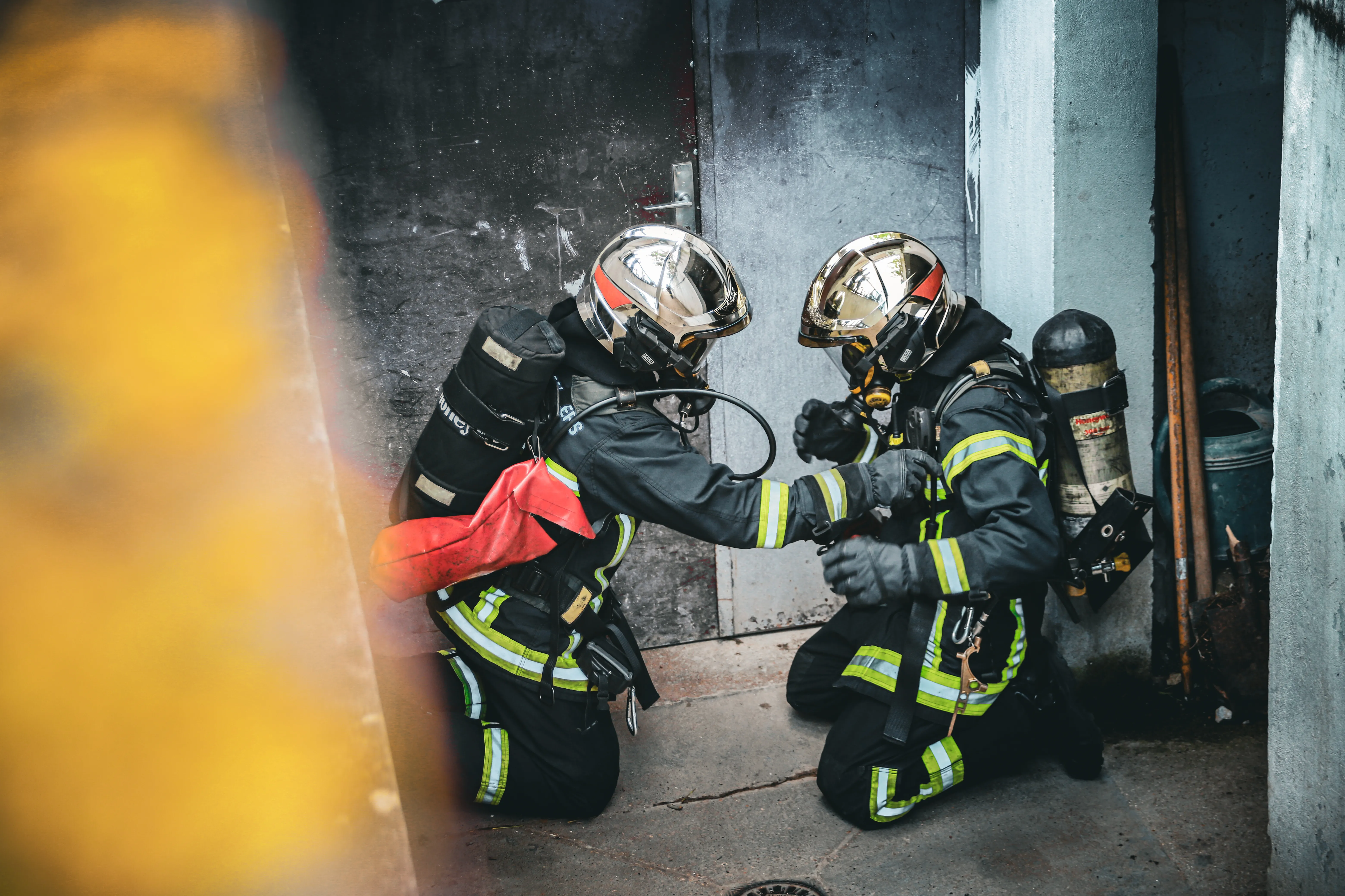 Un binôme de sapeurs-pompiers sous appareil respiratoire, à genoux avant d'entrer